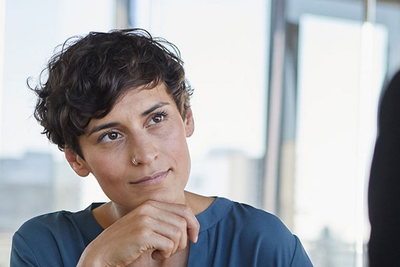 Frau mit dunklen, kurzen Haaren und mintfarbenem Shirt, sitzt vor einer Fensterfront vor einer Person