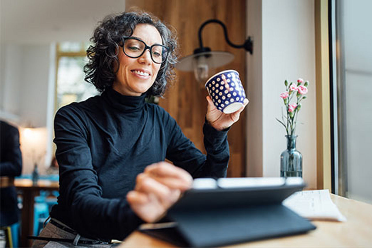 Frau mit Kaffeetasse arbeitet an einem Tablet
