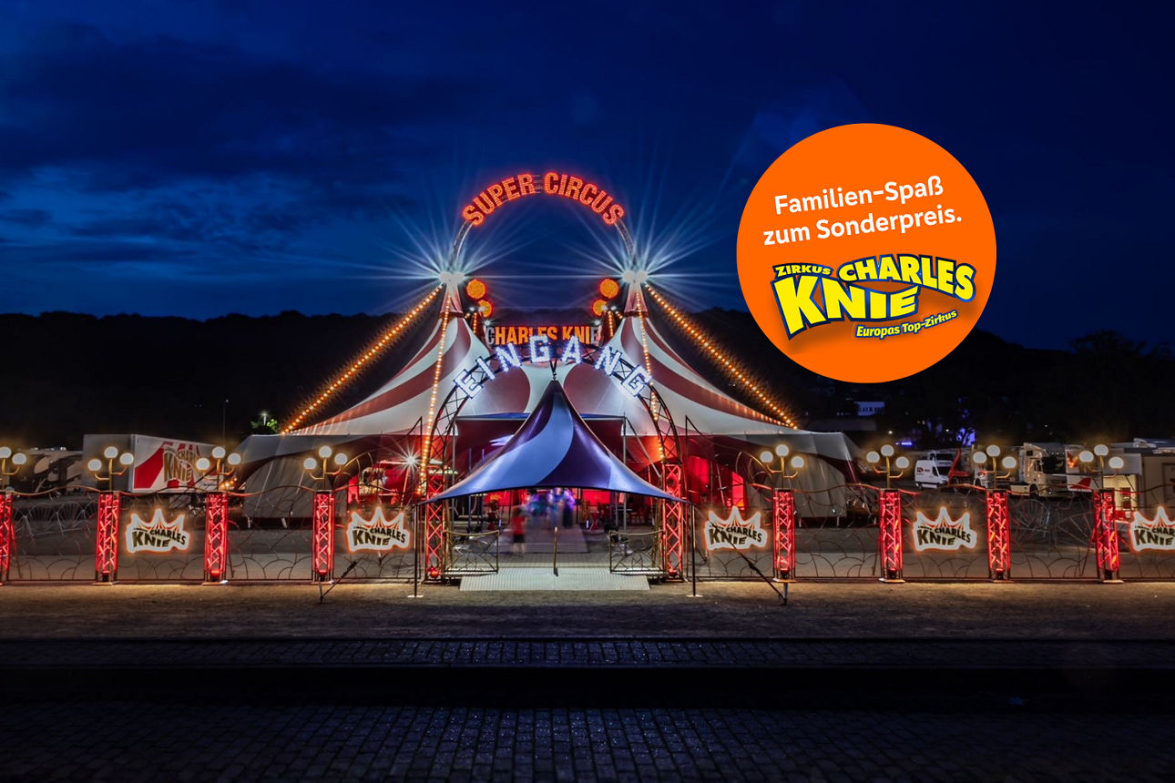 Beleuchtetes Zirkuszelt von Charles Knie bei Nacht, mit orangefarbigem Kreis für Familienspaß‑Sonderpreis.