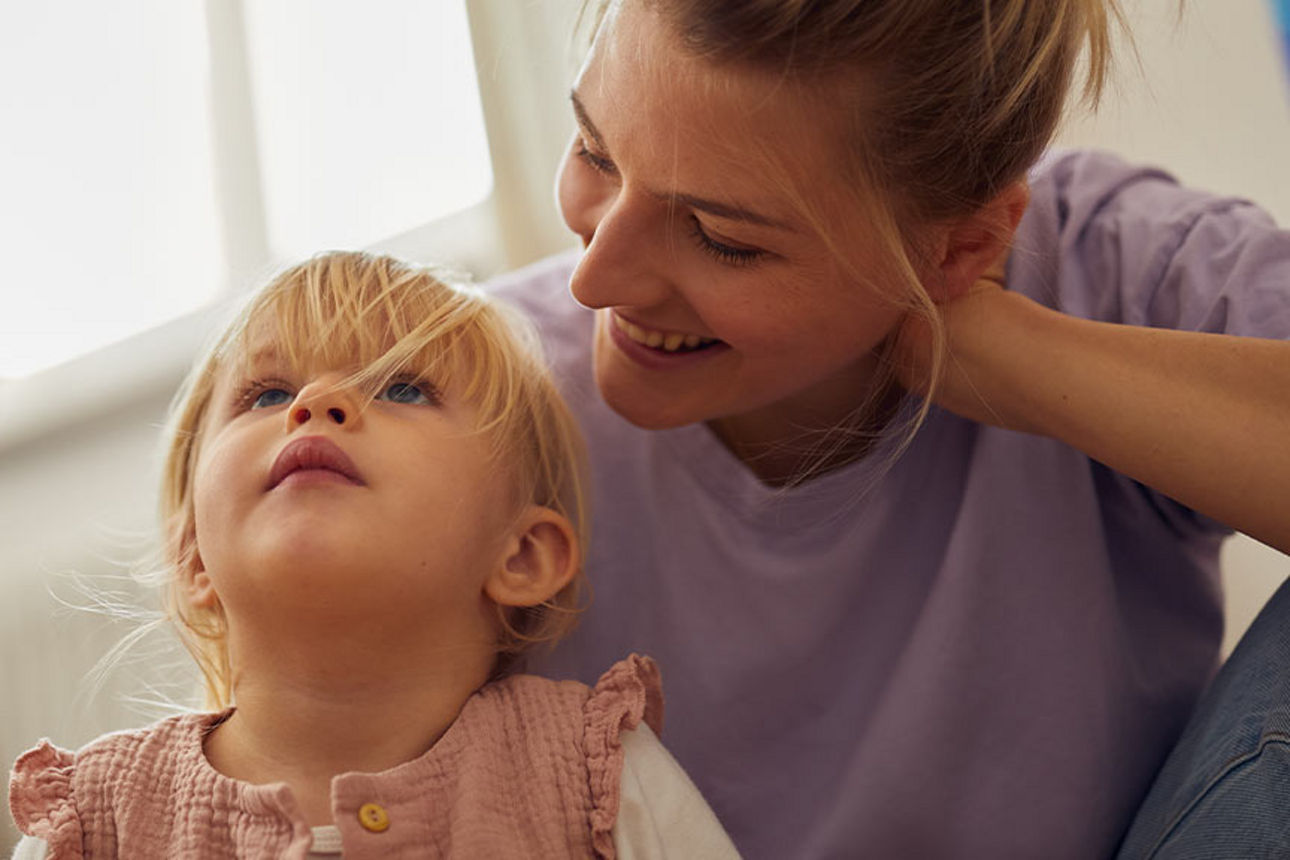 Mutter schaut kleine Tochter liebevoll von hinten an
