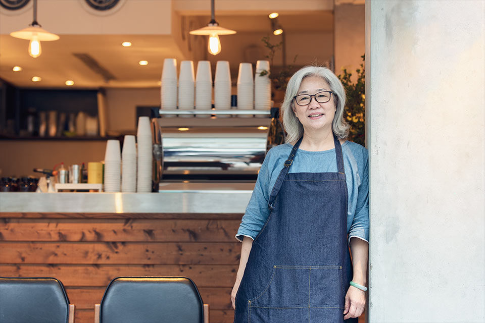 Frau steht in einem Café vor der Bar mit Kaffeemaschine- und blickt in die Kamera