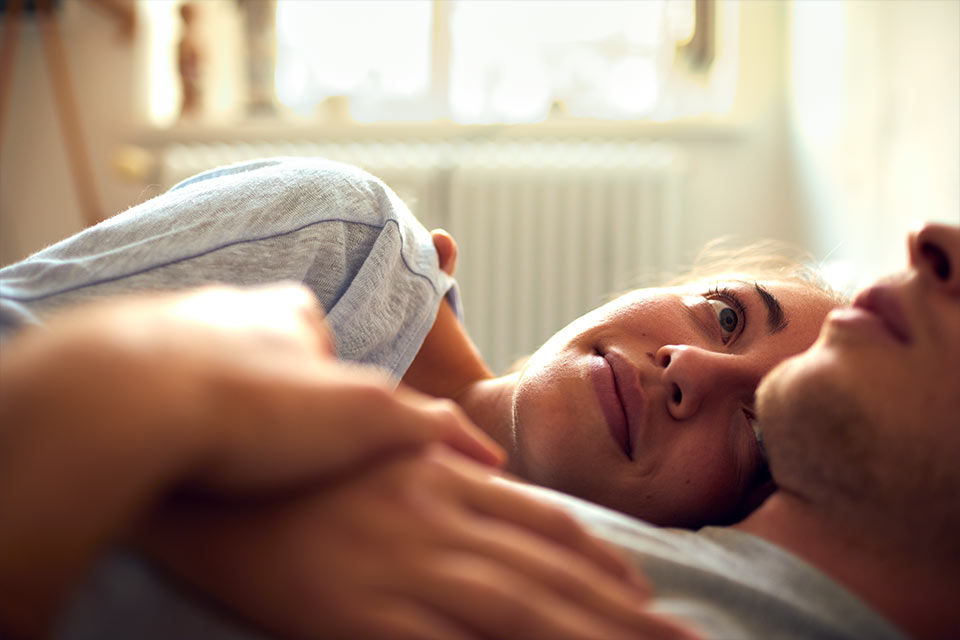 Junge Frau liegt im Arm ihres Partners und schaut ihn von der Seite an