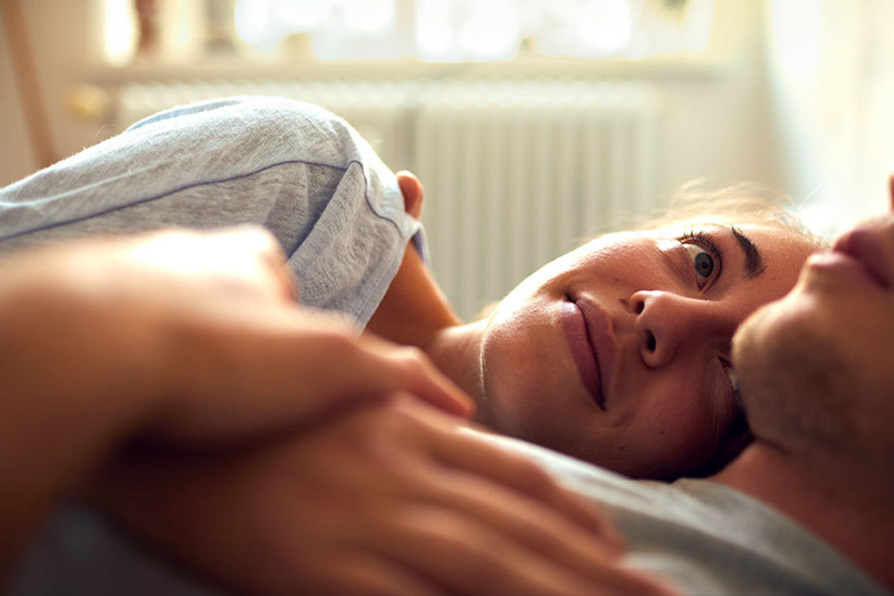 Junge Frau liegt im Arm ihres Partners und schaut ihn von der Seite an