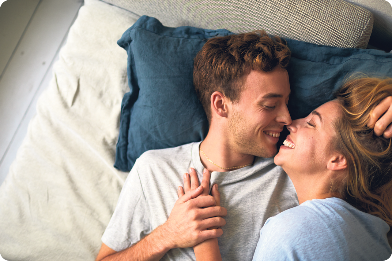 Ein junges Paar liegt auf dem Sofa und schaut sich glücklich an