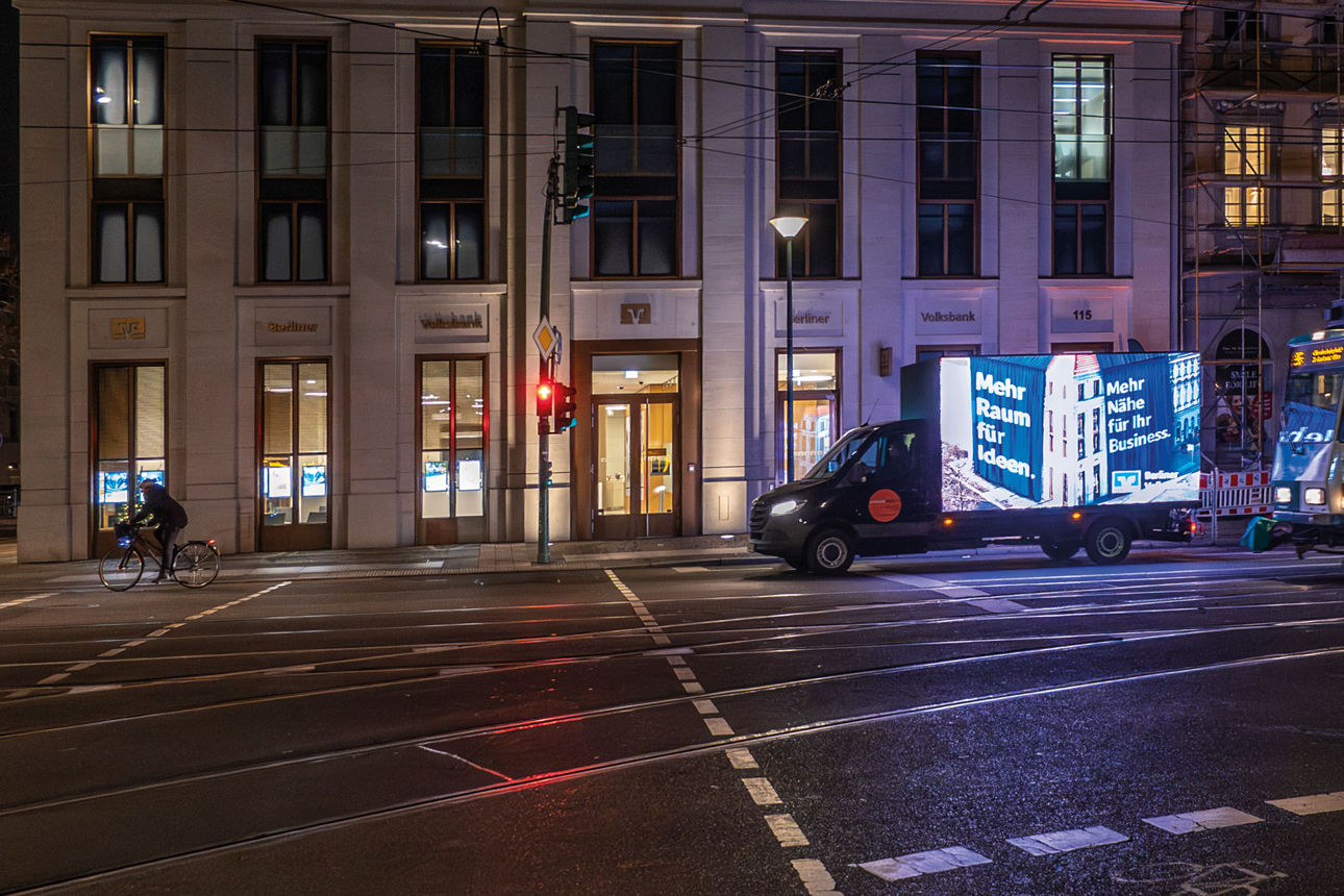 Nächtliche Straßenszene mit Straßenbahn und beleuchtetem Gebäude an einer Kreuzung.