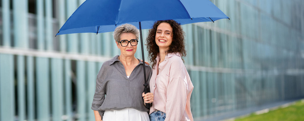 Zwei Frauen unter einem blauen Schirm vor einem Gebäude