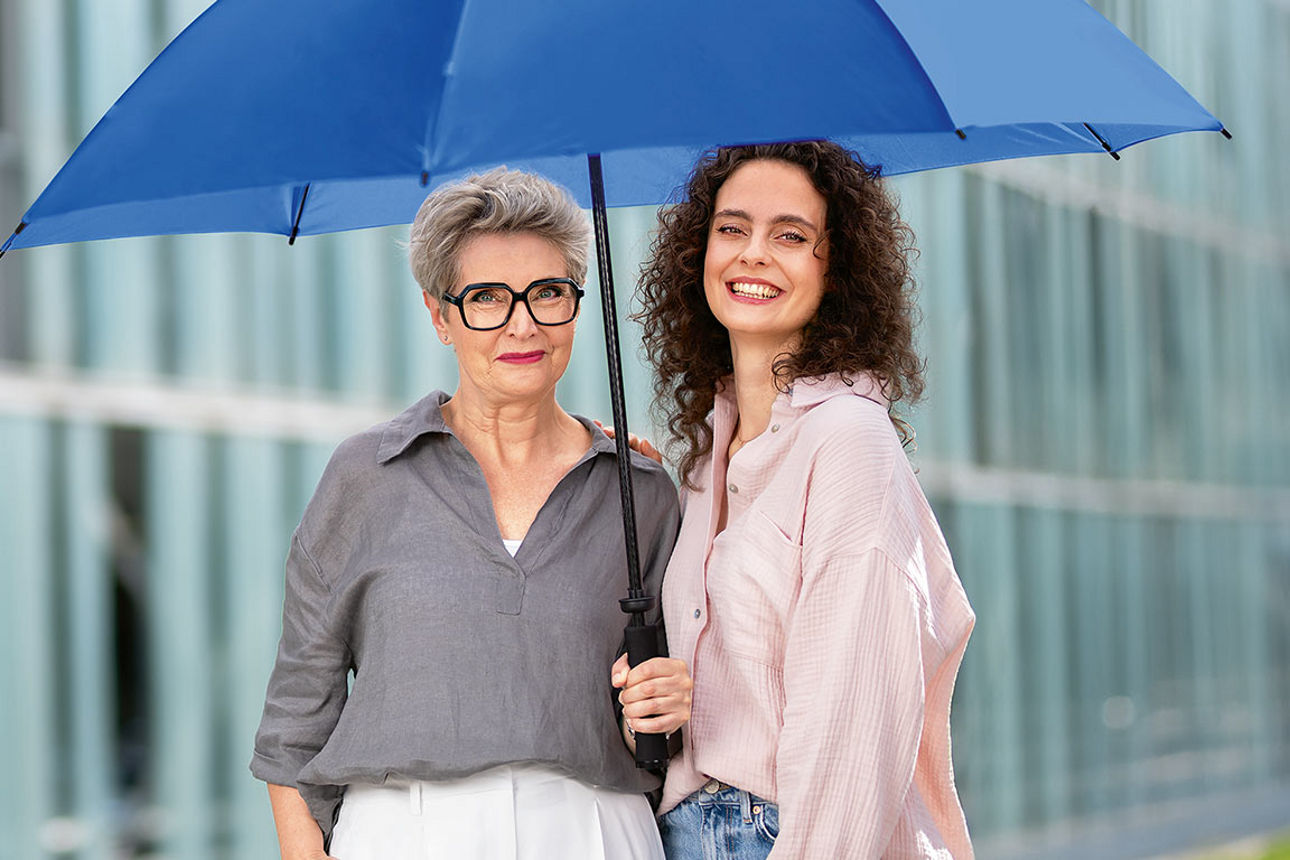 Zwei Frauen unter einem blauen Schirm vor einem Gebäude