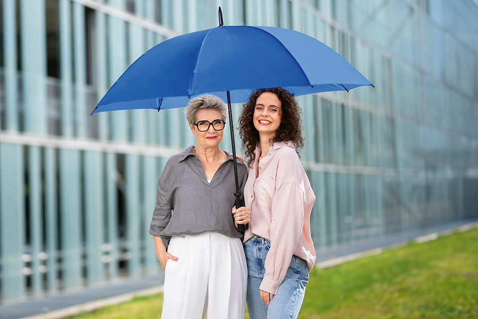 Zwei Frauen unter einem blauen Schirm vor einem Gebäude
