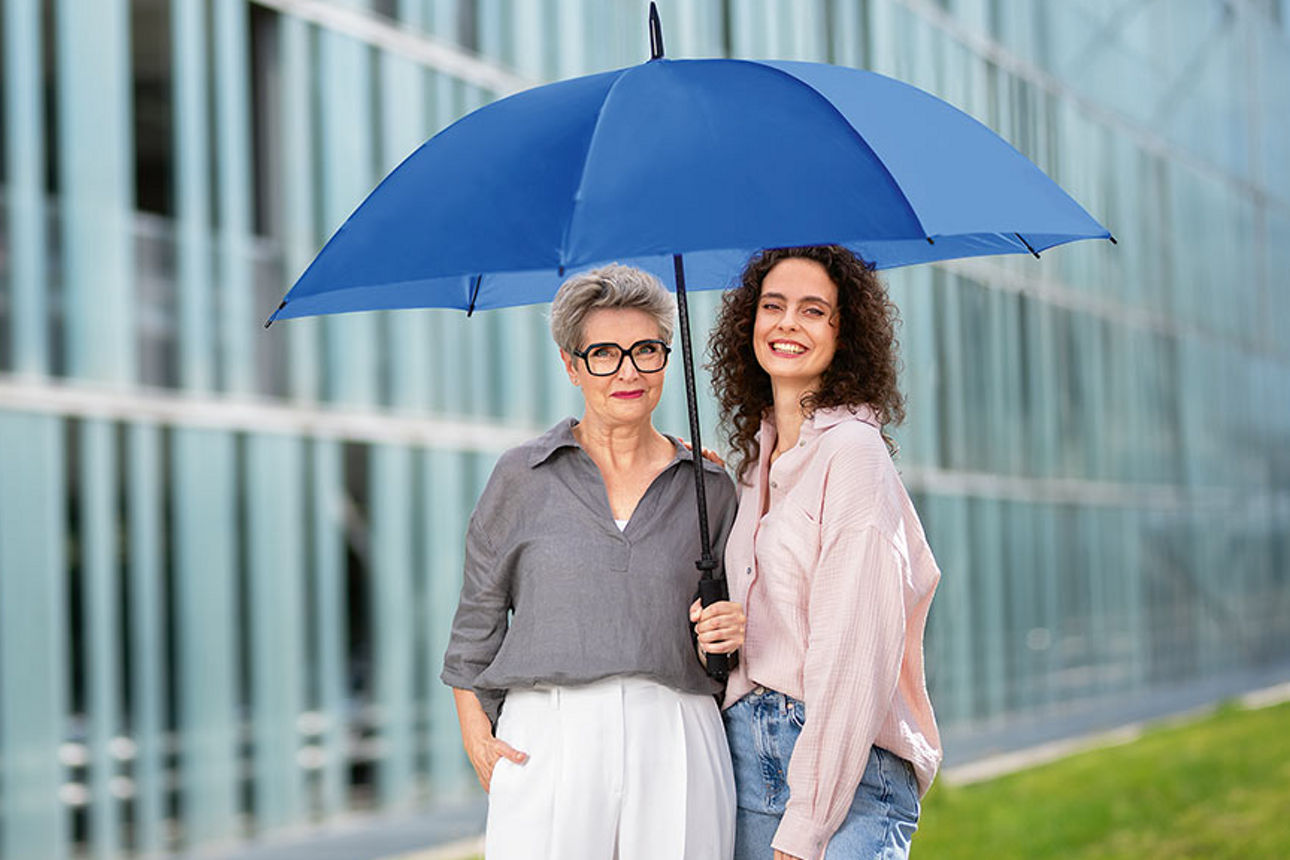 Zwei Frauen unter einem blauen Schirm vor einem Gebäude