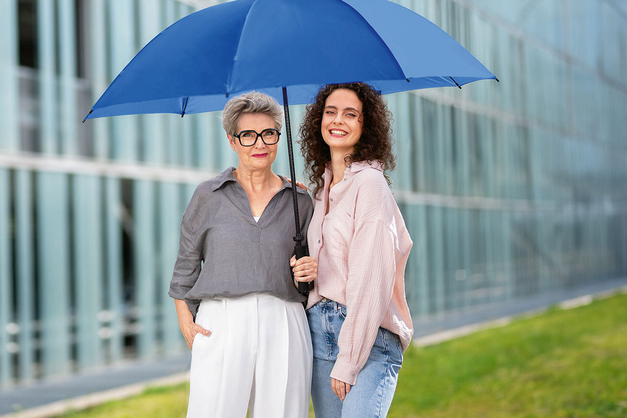 Zwei Frauen unter einem blauen Schirm vor einem Gebäude