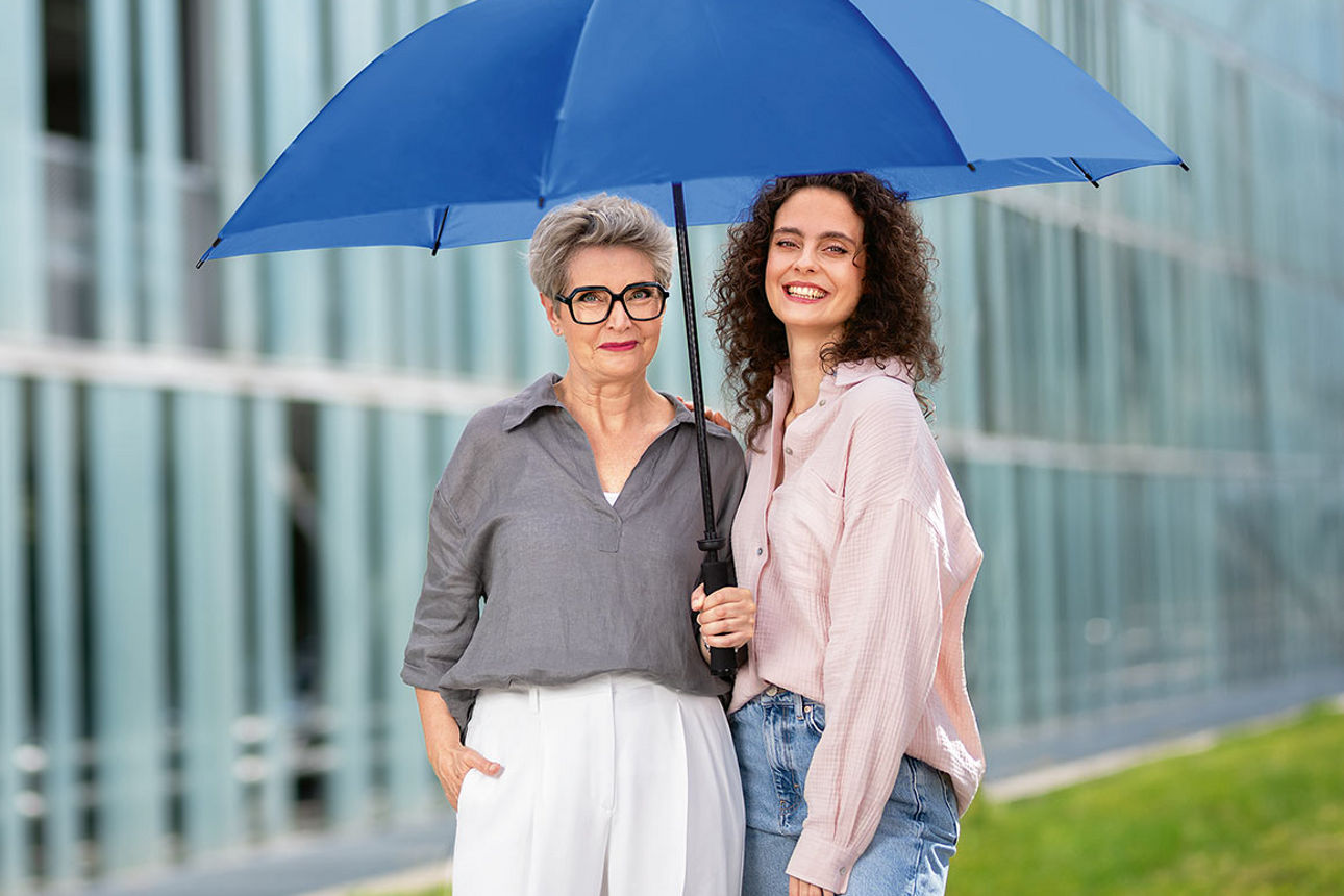 Zwei Frauen unter einem blauen Schirm vor einem Gebäude