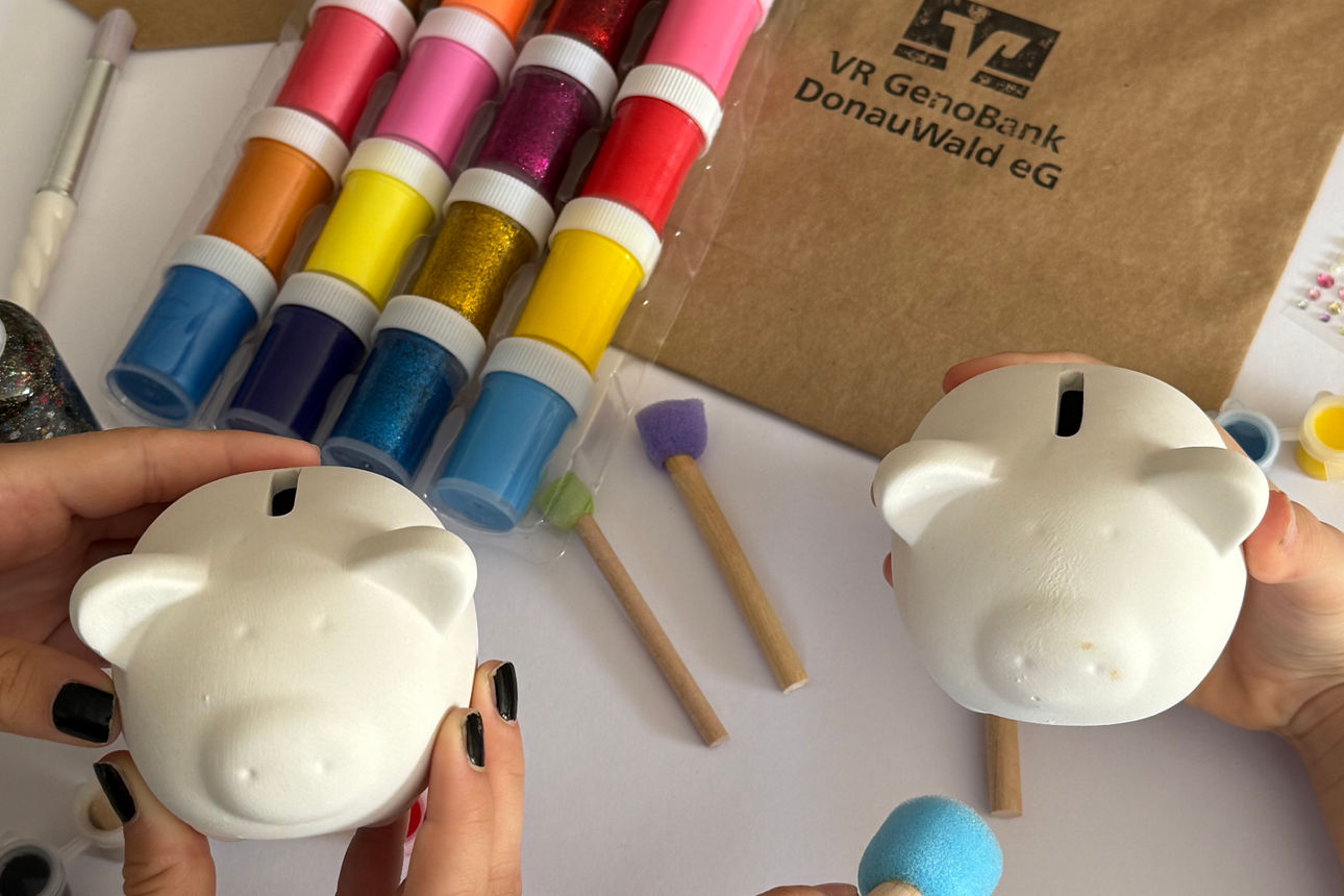 zwei weiße Sparscheine, daneben liegen bunte Farbdöschen und Pinsel